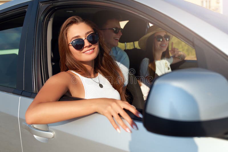 Group of friends rented a car on summer road trip and arrived to the sea beach. Woman in glasses looks out of the car