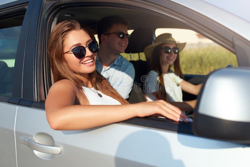 Group of friends rented a car on summer road trip and arrived to the sea beach. Woman in glasses looks out of the car