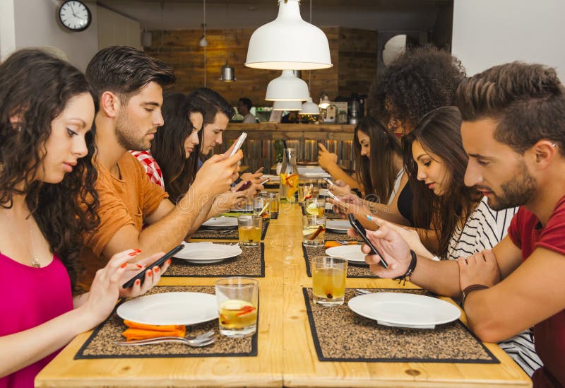 Social but not social. Group of friends at a restaurant with all people on the table occupied with cellphones royalty free stock image