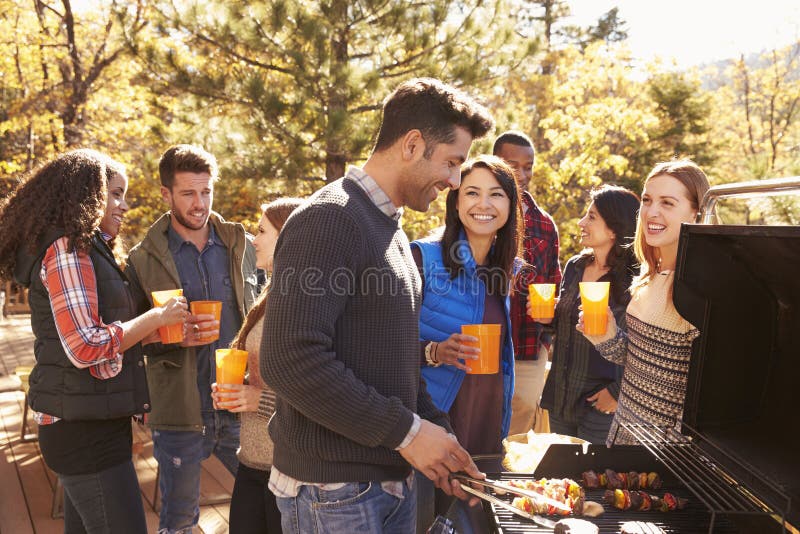 Group of friends stand at a barbecue, one cooking at grill royalty free stock image Group of friends stand at a barbecue, one cooking at grill royalty free stock image