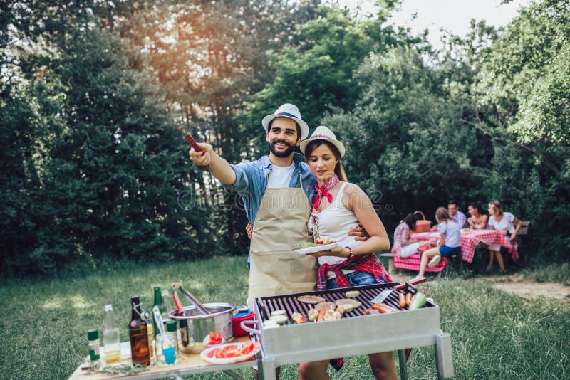 Friends stand at a barbecue, one cooking at grill royalty free stock image Friends stand at a barbecue, one cooking at grill royalty free stock image