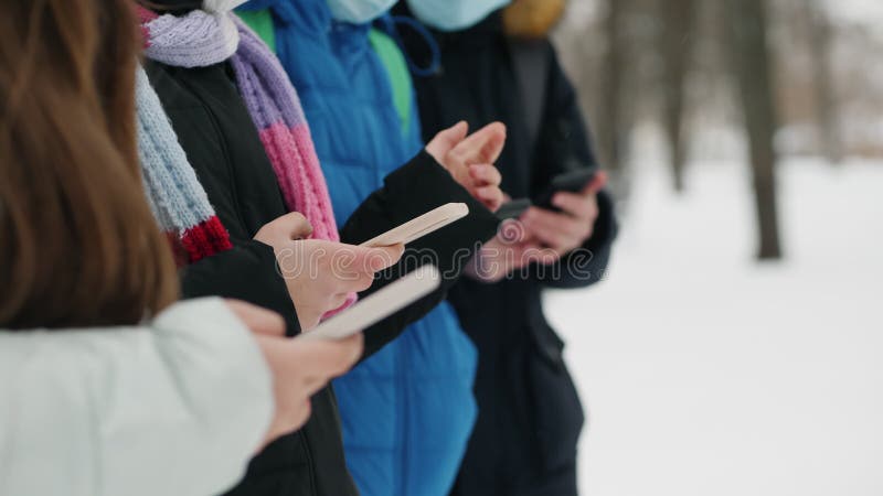 Group of friends use smartphones in winter, hands close-up