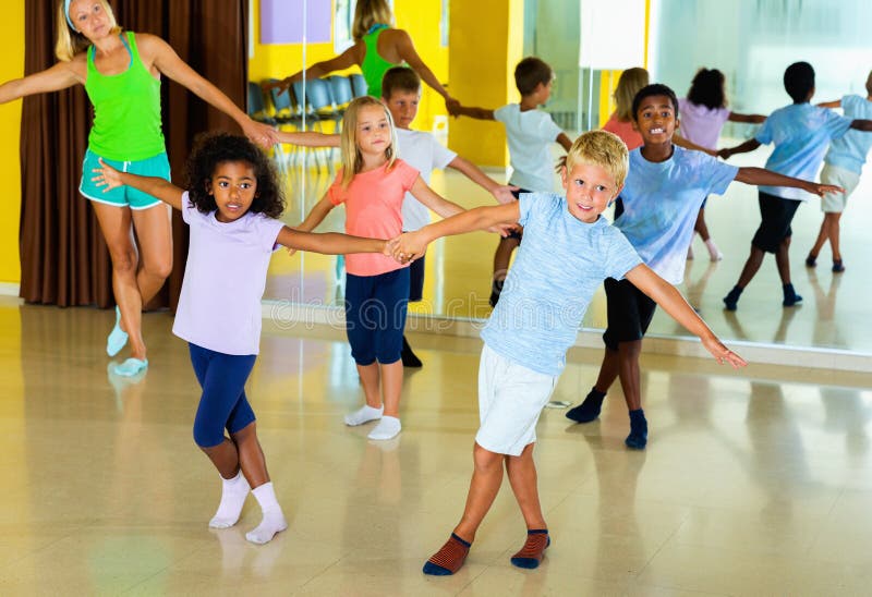 Group of Children Practicing Vigorous Jive Movements in Dance Class with Female Coach Stock