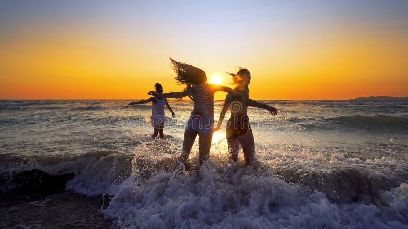 Group of happy girls jump over sea waves at the beach on sunset stock images Group of happy girls jump over sea waves at the beach on sunset stock images