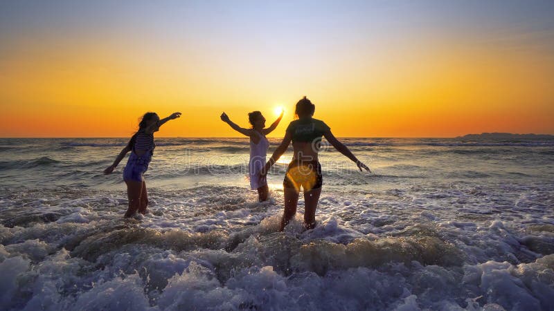 Group of happy girls jump over sea waves at the beach on sunset royalty free stock image Group of happy girls jump over sea waves at the beach on sunset royalty free stock image