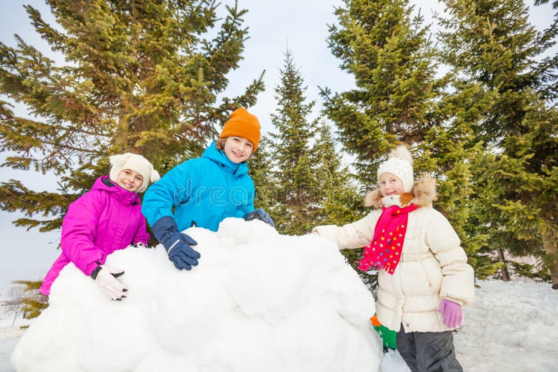 Group of happy kids build behind snow wall. Group of happy kids together building behind the snow wall with fir forest on the background during winter day royalty free stock photo