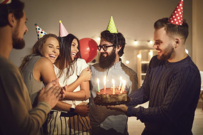 Happy Birthday, Beautiful Group of cheerful young people in conical party hats celebrating their friend`s birthday, giving her delicious cake with burning candles and wishing her all the best in life. Happy Birthday, Beautiful Group of cheerful young people in conical party hats celebrating their friend`s birthday, giving her delicious cake with burning candles and wishing her all the best in life