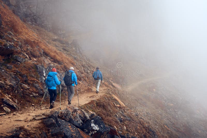 Group Hikers with Backpacks walking down on Mountain Trail in foggy mountains