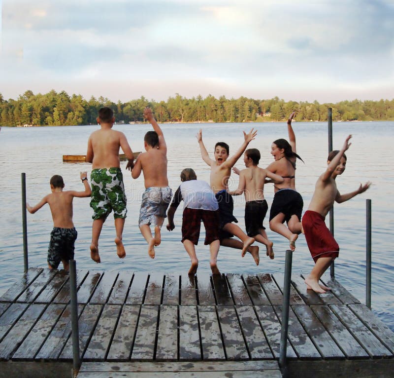 Un gruppo di otto bambini di età 11-13 saltando su un dock in un lago al campo estivo.