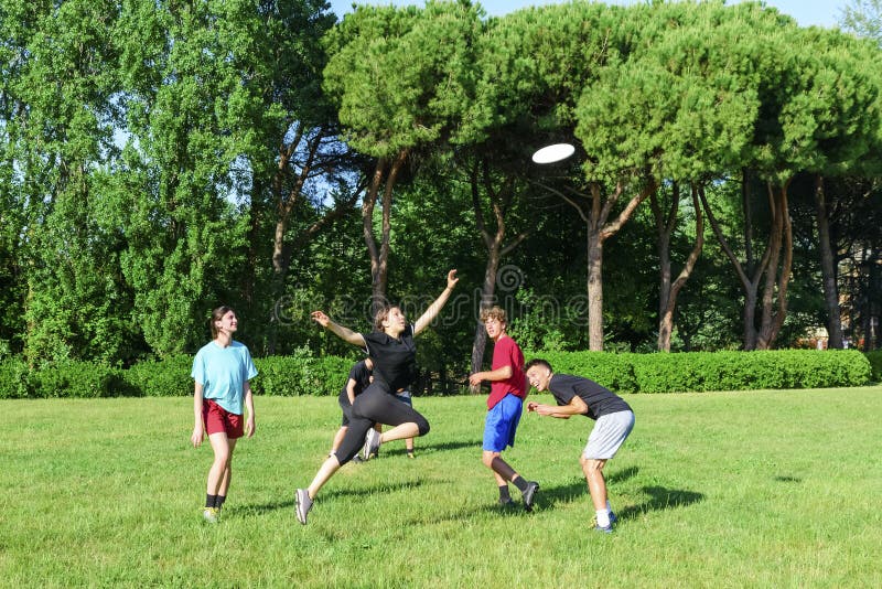 Group of mixed young teenagers people in casual wear playing with plastic flying disc game in a park oudoors. jumping woman catch