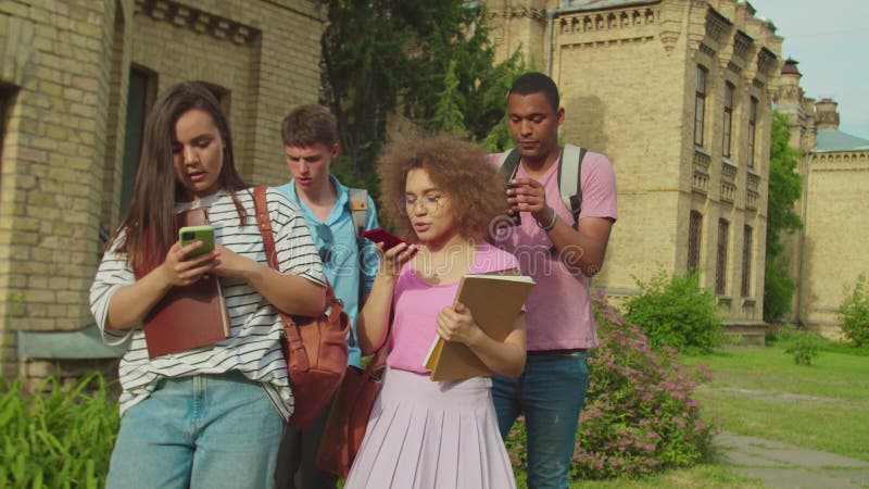 Diverse students obsessed with smartphones outdoors leaving classes