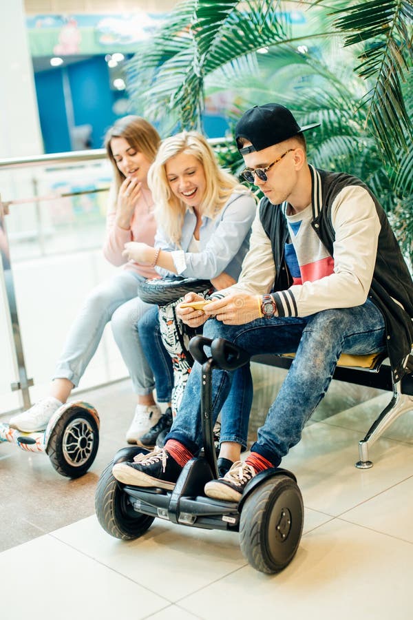 Group of people on electric scooter hoverboard sitting at bench and using phone stock photo Group of people on electric scooter hoverboard sitting at bench and using phone stock photo
