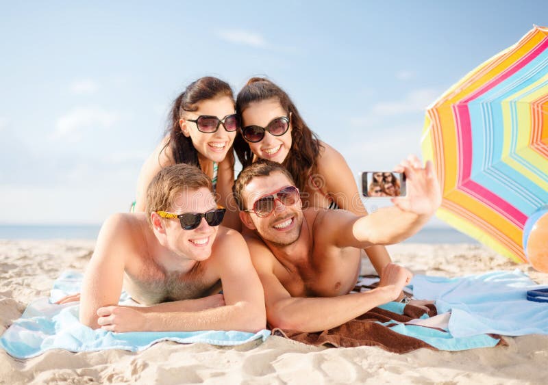 Estate, vacanze, vacanza, la tecnologia e la felicità concetto di gruppo di persone sorridenti in occhiali da sole per scattare foto con lo smartphone sulla spiaggia.