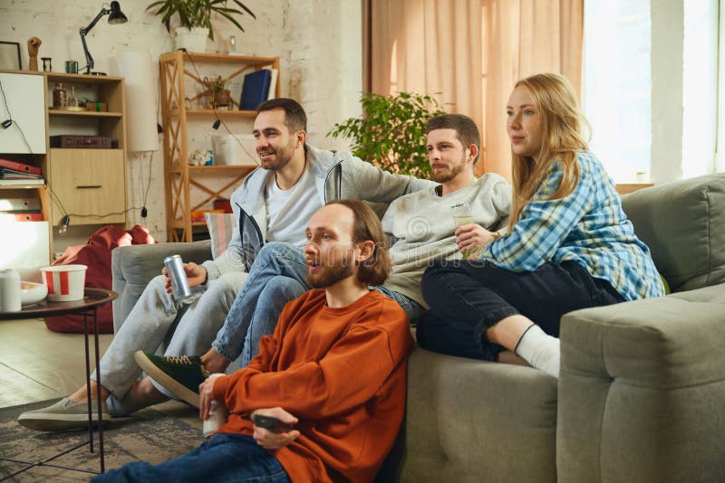 Group portrait. Guys and girl sitting in living room and spending all time watching new films with an exciting stock photo
