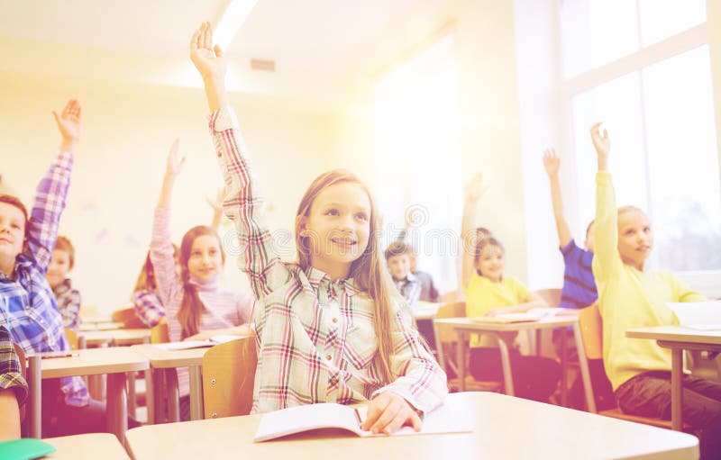 Group of school kids raising hands in classroom royalty free stock images