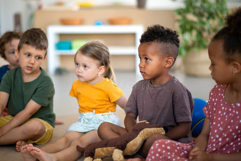 Group Of Small Nursery School Children Sitting On Floor Indoors In