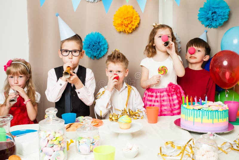 Funny birthday games. Group of smiling children playing on the birthday party in decorated room. Happy kids blowing in pipes on birthday party stock image Funny birthday games. Group of smiling children playing on the birthday party in decorated room. Happy kids blowing in pipes on birthday party stock image