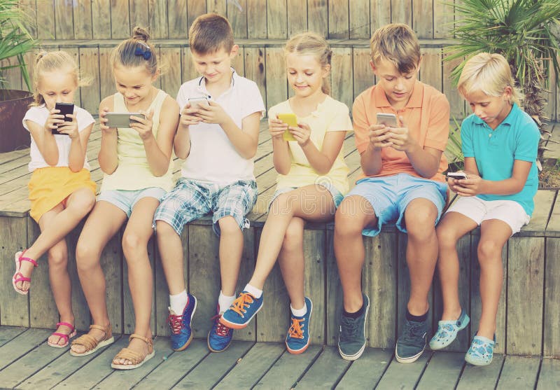 Group of Smiling Children Playing with Mobile Phones Outdoors Stock