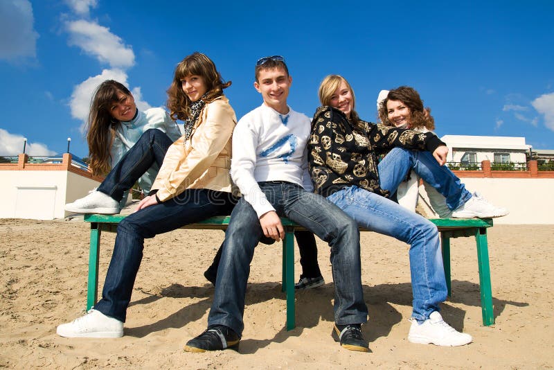 Group smiling teenagers sitting on a bench