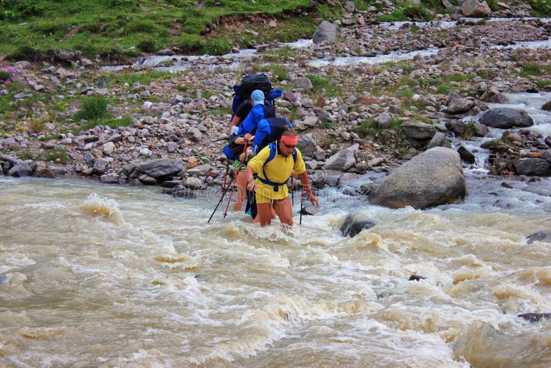 A group of tourists passes a rough mountain river for a wade.