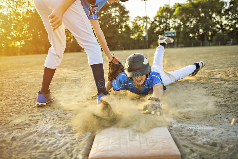 Group of two baseball players play together on the playground. On of them slide on the goal