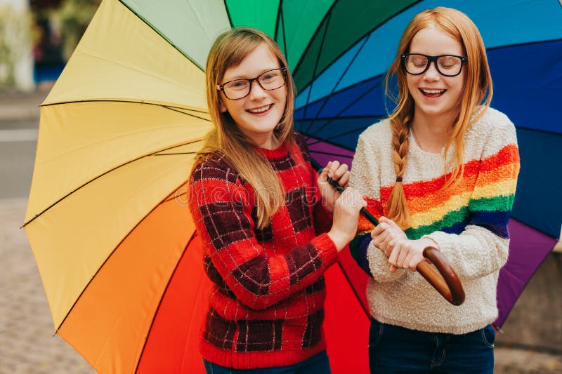 Group of two cute little girls playing outside under big colorful umbrella