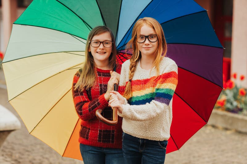 Group of two cute little girls playing outside under big colorful umbrella