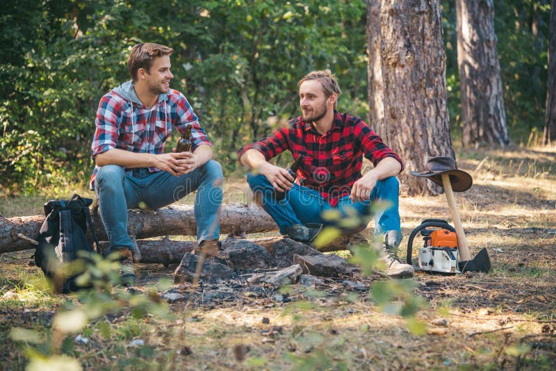 Group of two male backpackers relaxing near campfire. Young man having picnic in woods. Friends sit on forest picnic stock photo Group of two male backpackers relaxing near campfire. Young man having picnic in woods. Friends sit on forest picnic stock photo