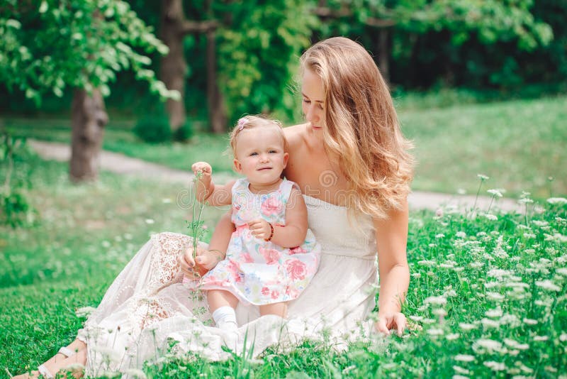 Group of two people, white Caucasian mother and baby girl child in white dress sitting playing in green summer park forest outside royalty free stock images Group of two people, white Caucasian mother and baby girl child in white dress sitting playing in green summer park forest outside royalty free stock images