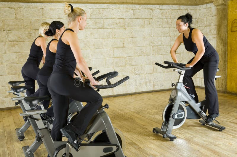 The group of women in dark sportswear training on exercise bike at the gym. Side view. The group of women in dark sportswear training on exercise bike at the gym. Side view.