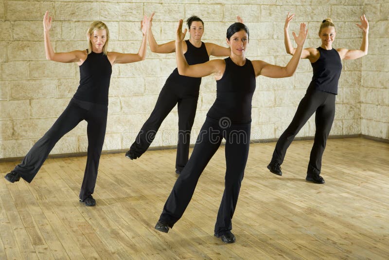 A group of women exercising in the fitness club. They're smiling and looking at camera. They have hands up. Front view. A group of women exercising in the fitness club. They're smiling and looking at camera. They have hands up. Front view.