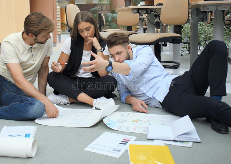 Group of young business people and designers looking at project plan laid out on floor. They working on new project. stock photo Group of young business people and designers looking at project plan laid out on floor. They working on new project. stock photo