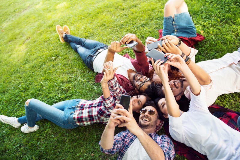 Group of young people laying on the grass in circle, thumbs upGroup of young people laying on the grass in circle, using phones