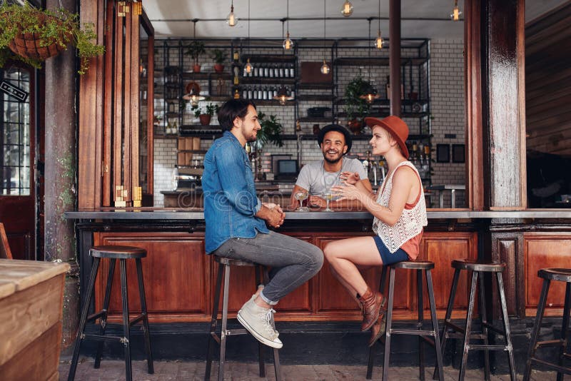 Portrait of happy group of young people meeting in a coffee shop and talking. Three young friends sitting at a cafe table.