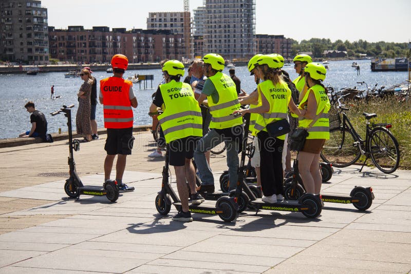 Group of young people on scooter guided sightseeing tour is stopping by an urban harbor in sunny weathersun, looking, travel, buildings. Copenhagen, Denmark - June 5, 2021