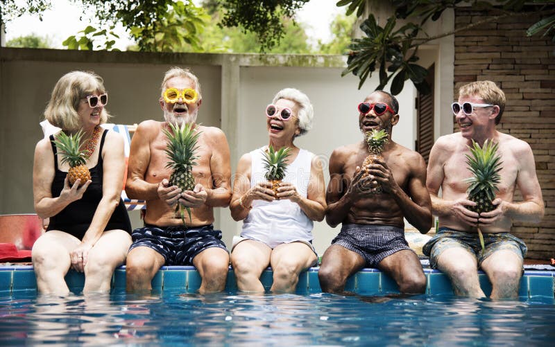 Groupe d'adultes supérieurs divers s'asseyant au poolside tenant le pinea image stock Groupe d'adultes supérieurs divers s'asseyant au poolside tenant le pinea image stock