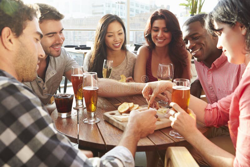 Groupe d'amis appréciant la boisson et le casse-croûte dans la barre de dessus de toit images libres de droits Groupe d'amis appréciant la boisson et le casse-croûte dans la barre de dessus de toit images libres de droits