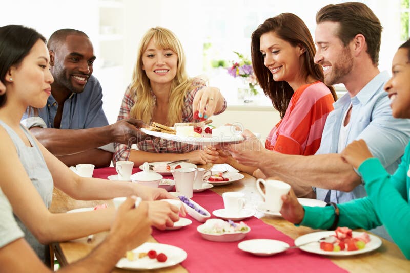 Group Of Friends Having Cheese And Coffee At Dinner Party Sitting Around Table Helping Themselves To Food. Group Of Friends Having Cheese And Coffee At Dinner Party Sitting Around Table Helping Themselves To Food