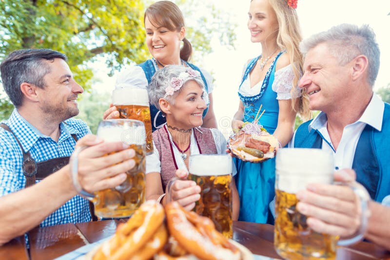 Group of friends in beer garden toasting to camera wearing Bavarian tracht. Group of friends in beer garden toasting to camera wearing Bavarian tracht