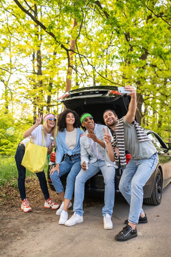 Groupe d'amis faisant du selfie dans la forêt assis sur la botte de voiture image stock