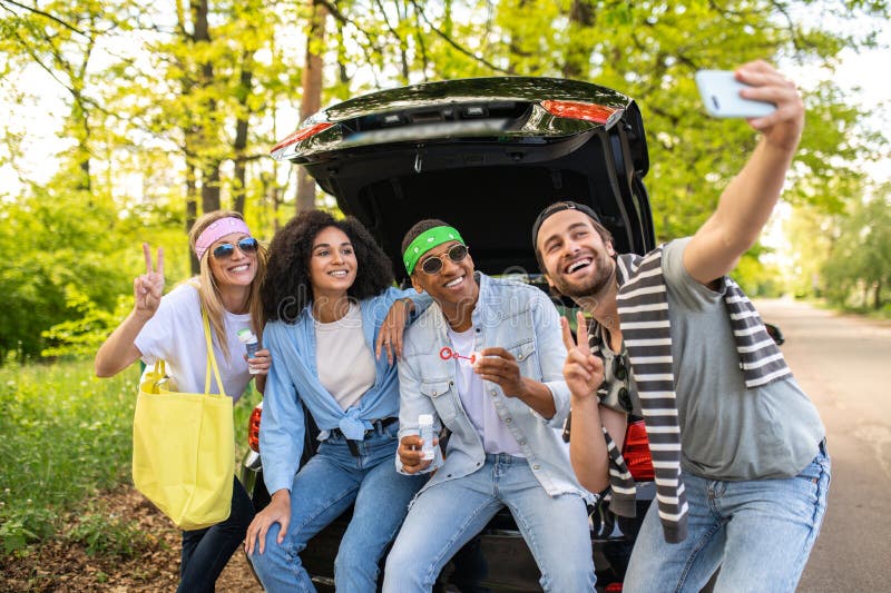 Groupe d'amis faisant du selfie dans la forêt assis sur la botte de voiture photo libre de droits