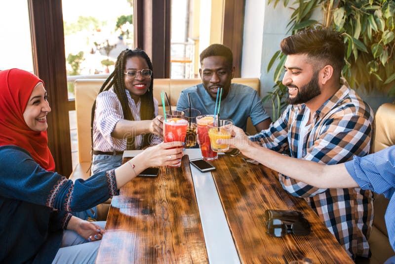 Groupe d'amis heureux faisant tinter des verres avec du jus au café photos stock Groupe d'amis heureux faisant tinter des verres avec du jus au café photos stock