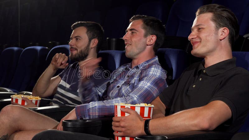 Cheerful young men talking, eating popcorn, enjoying watching movies at the cinema together. Male friends relaxing at the movie theatre. Friendship, lifestyle, happiness concept. Cheerful young men talking, eating popcorn, enjoying watching movies at the cinema together. Male friends relaxing at the movie theatre. Friendship, lifestyle, happiness concept.