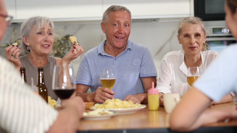 Groupe d'amis personnes âgées joyeuses femmes et homme se rassemblant autour de la table de cuisine pour déguster de la bière et d banque de vidéos