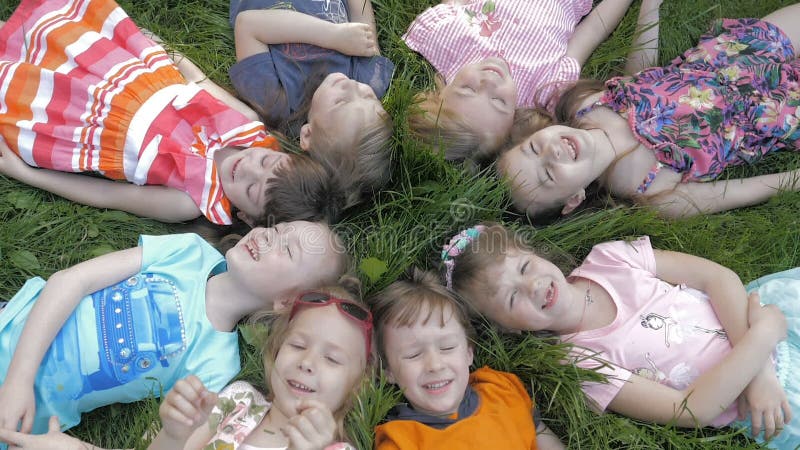 Groupe d'enfants heureux allongés sur l'herbe verte en plein air dans le parc de printemps clips vidéos