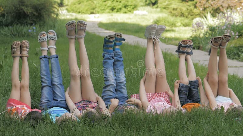 Groupe d'enfants heureux allongés sur l'herbe verte en plein air dans le parc de printemps banque de vidéos