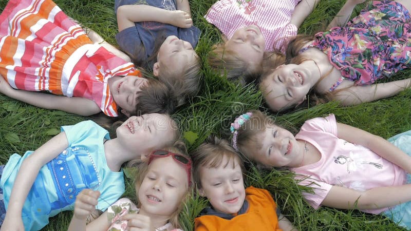 Groupe d'enfants heureux allongés sur l'herbe verte en plein air dans le parc de printemps banque de vidéos