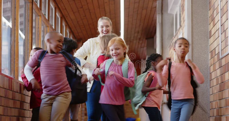 Groupe d'écoliers marchant dans un couloir avec des sacs à dos souriants et parlant banque de vidéos