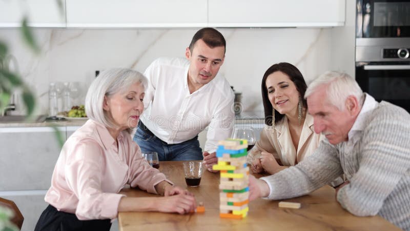 Groupe d'épouses matures et fils avec petite amie joue jeu de société avec des blocs en bois dans la cuisine banque de vidéos
