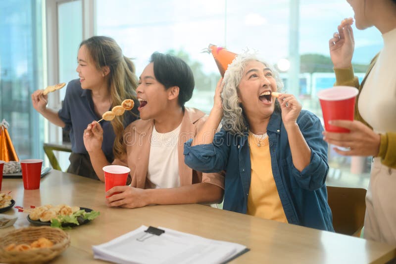 Groupe de collègues joyeux se sont rassemblés autour de table pour déguster des collations et des boissons pendant la fête décontr image stock